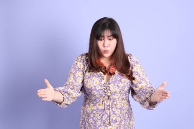 Mor arka planda sıradan kıyafetlerle duran tombul Asyalı kadın..