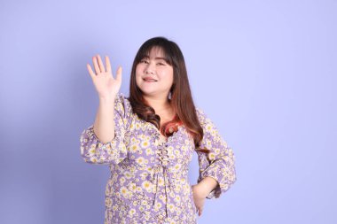 Mor arka planda sıradan kıyafetlerle duran tombul Asyalı kadın..