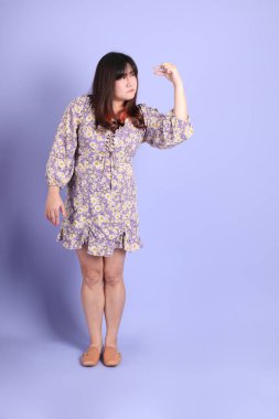 Mor arka planda sıradan kıyafetlerle duran tombul Asyalı kadın..