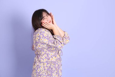 Mor arka planda sıradan kıyafetlerle duran tombul Asyalı kadın..