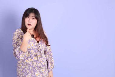 Mor arka planda sıradan kıyafetlerle duran tombul Asyalı kadın..