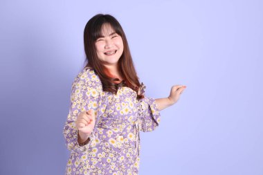 Mor arka planda sıradan kıyafetlerle duran tombul Asyalı kadın..