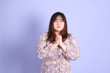 Mor arka planda sıradan kıyafetlerle duran tombul Asyalı kadın..