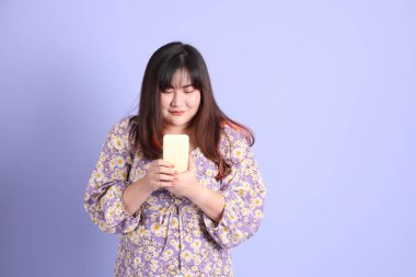 Mor arka planda sıradan kıyafetlerle duran tombul Asyalı kadın..