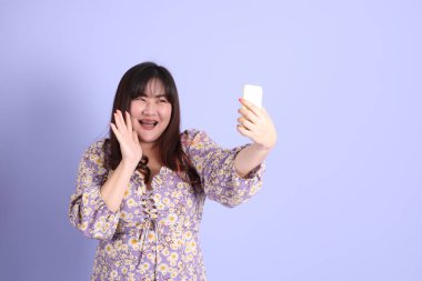 Mor arka planda sıradan kıyafetlerle duran tombul Asyalı kadın..