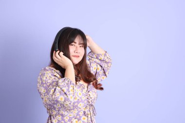 Mor arka planda sıradan kıyafetlerle duran tombul Asyalı kadın..