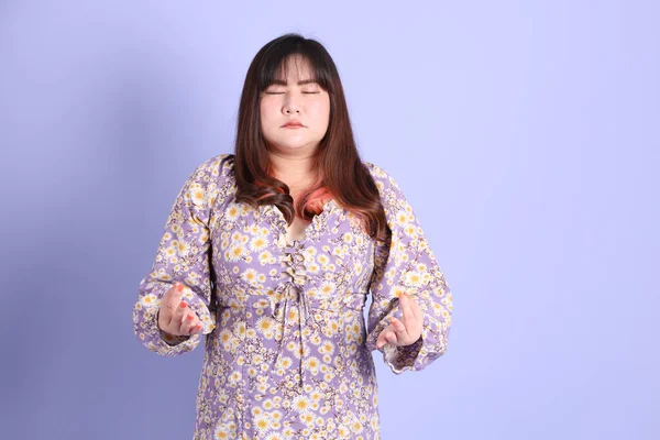 Mor arka planda sıradan kıyafetlerle duran tombul Asyalı kadın..