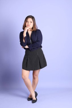 The chubby Asian woman standing on the purple background with the casual clothes.