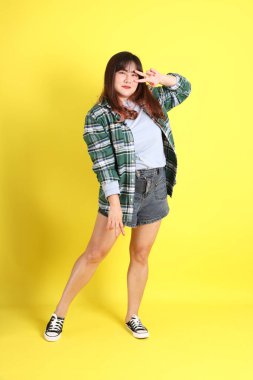 Sarı arka planda sıradan kıyafetlerle duran tombul Asyalı kadın..