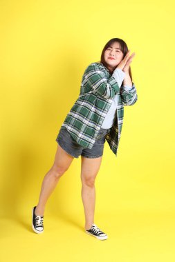 Sarı arka planda sıradan kıyafetlerle duran tombul Asyalı kadın..