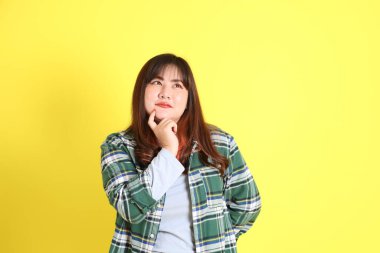 Sarı arka planda sıradan kıyafetlerle duran tombul Asyalı kadın..