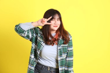 Sarı arka planda sıradan kıyafetlerle duran tombul Asyalı kadın..