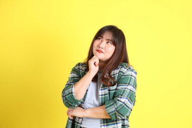 The chubby Asian woman standing on the yellow background with the casual clothes.