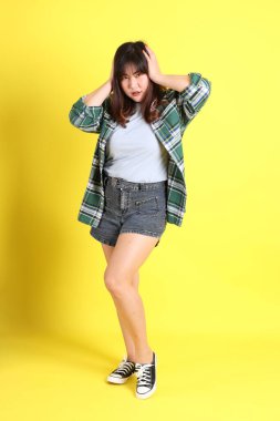 Sarı arka planda sıradan kıyafetlerle duran tombul Asyalı kadın..