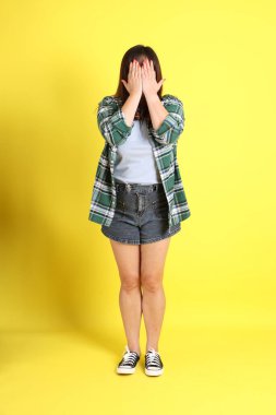 Sarı arka planda sıradan kıyafetlerle duran tombul Asyalı kadın..