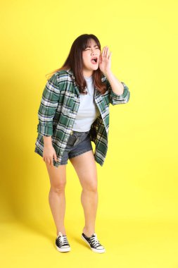 Sarı arka planda sıradan kıyafetlerle duran tombul Asyalı kadın..