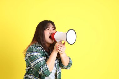 The chubby Asian woman standing on the yellow background with the casual clothes.