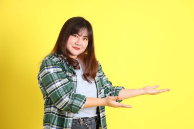 Sarı arka planda sıradan kıyafetlerle duran tombul Asyalı kadın..