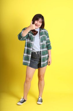 Sarı arka planda sıradan kıyafetlerle duran tombul Asyalı kadın..