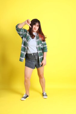 Sarı arka planda sıradan kıyafetlerle duran tombul Asyalı kadın..