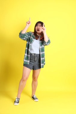 Sarı arka planda sıradan kıyafetlerle duran tombul Asyalı kadın..