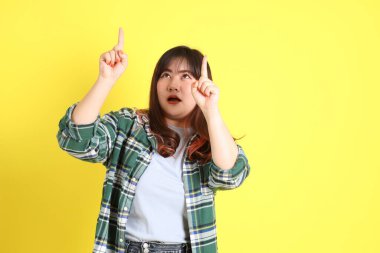 Sarı arka planda sıradan kıyafetlerle duran tombul Asyalı kadın..