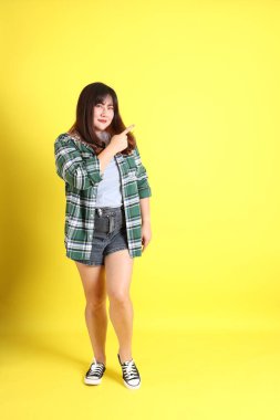 Sarı arka planda sıradan kıyafetlerle duran tombul Asyalı kadın..