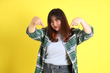 Sarı arka planda sıradan kıyafetlerle duran tombul Asyalı kadın..