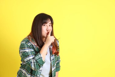 Sarı arka planda sıradan kıyafetlerle duran tombul Asyalı kadın..