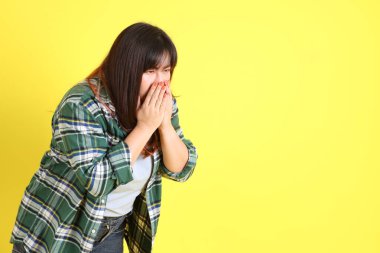 Sarı arka planda sıradan kıyafetlerle duran tombul Asyalı kadın..