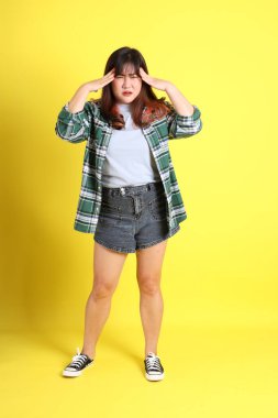 Sarı arka planda sıradan kıyafetlerle duran tombul Asyalı kadın..