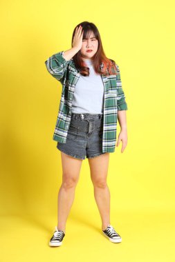 Sarı arka planda sıradan kıyafetlerle duran tombul Asyalı kadın..