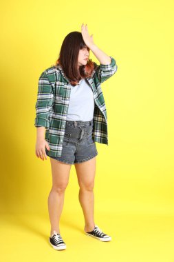 Sarı arka planda sıradan kıyafetlerle duran tombul Asyalı kadın..