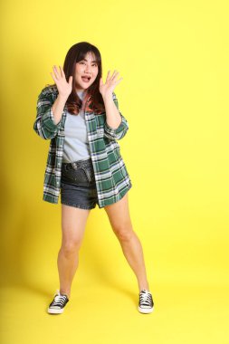 Sarı arka planda sıradan kıyafetlerle duran tombul Asyalı kadın..