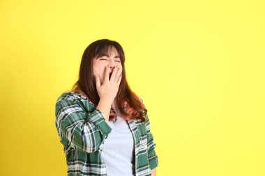 Sarı arka planda sıradan kıyafetlerle duran tombul Asyalı kadın..