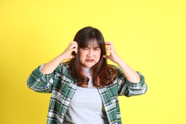 Sarı arka planda sıradan kıyafetlerle duran tombul Asyalı kadın..