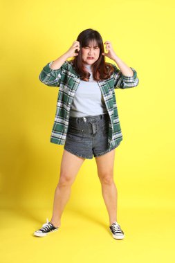 Sarı arka planda sıradan kıyafetlerle duran tombul Asyalı kadın..