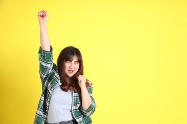 Sarı arka planda sıradan kıyafetlerle duran tombul Asyalı kadın..