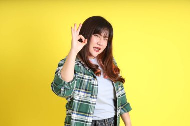 Sarı arka planda sıradan kıyafetlerle duran tombul Asyalı kadın..