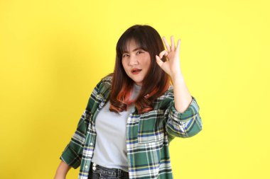 Sarı arka planda sıradan kıyafetlerle duran tombul Asyalı kadın..