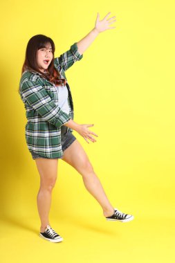 Sarı arka planda sıradan kıyafetlerle duran tombul Asyalı kadın..