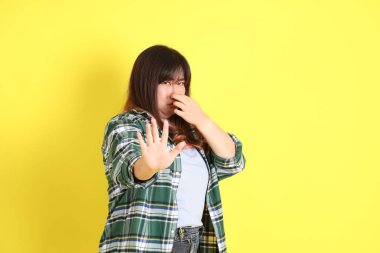 Sarı arka planda sıradan kıyafetlerle duran tombul Asyalı kadın..