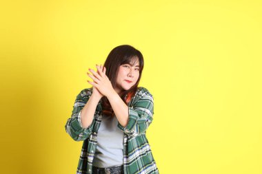 Sarı arka planda sıradan kıyafetlerle duran tombul Asyalı kadın..