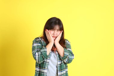 Sarı arka planda sıradan kıyafetlerle duran tombul Asyalı kadın..