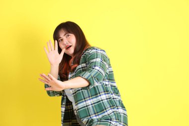 The chubby Asian woman standing on the yellow background with the casual clothes.