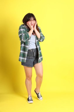 Sarı arka planda sıradan kıyafetlerle duran tombul Asyalı kadın..