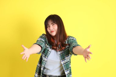 Sarı arka planda sıradan kıyafetlerle duran tombul Asyalı kadın..