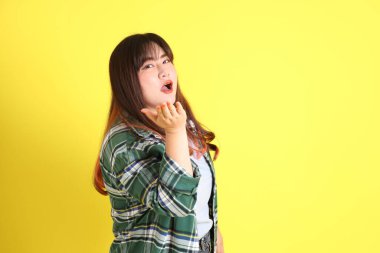 Sarı arka planda sıradan kıyafetlerle duran tombul Asyalı kadın..