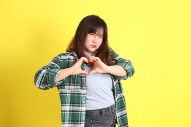 Sarı arka planda sıradan kıyafetlerle duran tombul Asyalı kadın..