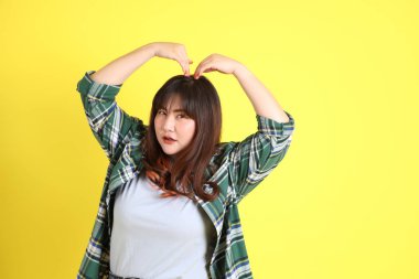 Sarı arka planda sıradan kıyafetlerle duran tombul Asyalı kadın..